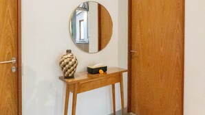 A hallway with two wooden doors, a small wooden console table with a vase and a mirror, and a tiled floor. - Singgah di Ubud 1 (Ubud)