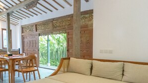 A modern living room with a sectional sofa, a round wooden coffee table, and a dining area with wooden chairs and a table. - Singgah di Ubud 1 (Ubud)