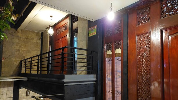 A staircase with a metal railing, a small table with a teapot and cup, and a wooden door with intricate carvings. - Dewi House Pondok Hijau Parongpong Bandung 1 (Parongpong)