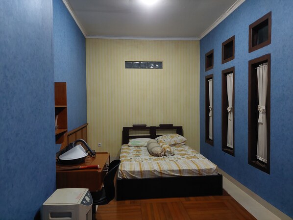 A bedroom with a bed, a desk with a computer, a heater, and a window with curtains.