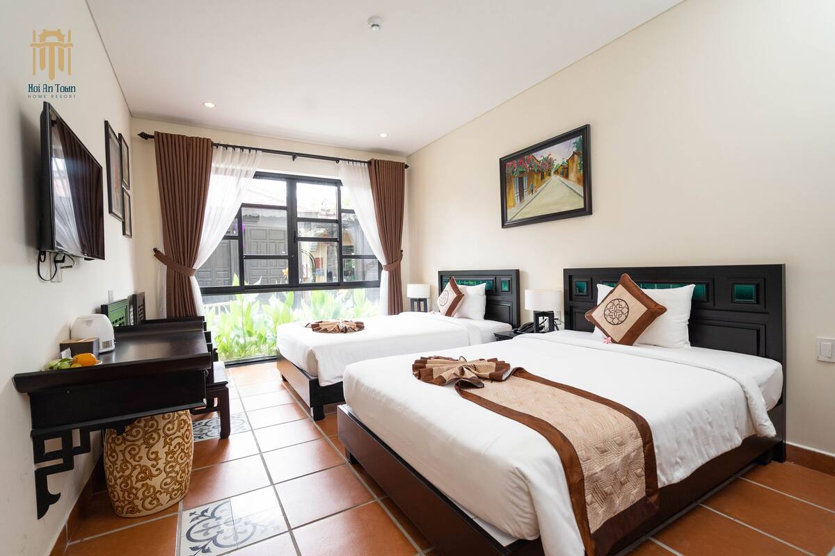 A hotel room with two beds, a desk, a TV, and a window with curtains.