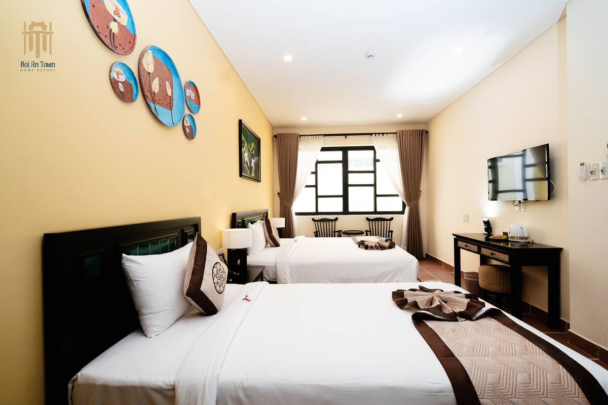 A hotel room with two beds, a TV, a desk, and a window with curtains.