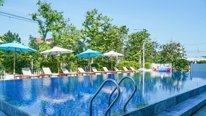 A swimming pool with lounge chairs and umbrellas, surrounded by trees. - Hoi An Town Home Resort (Da Nang)