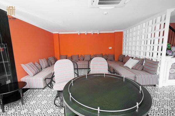 A room with a sectional sofa, a round table, patterned flooring, and a white partition.