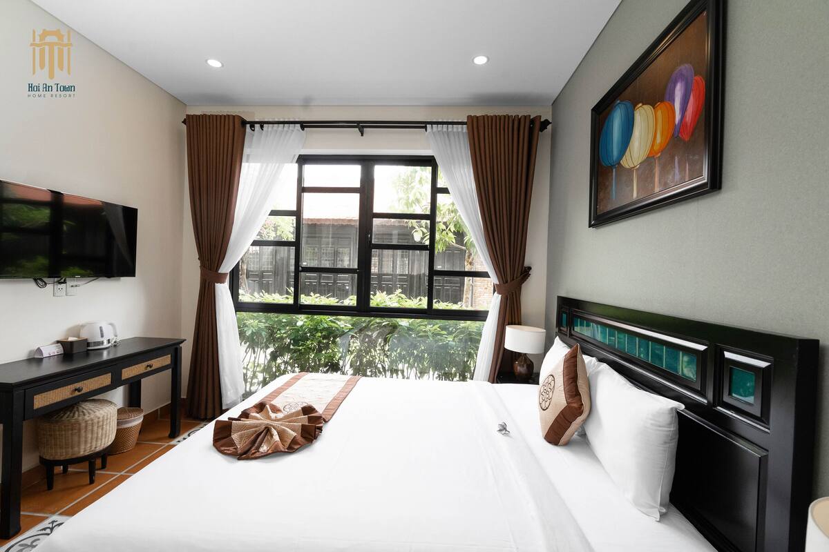 A hotel room with a bed, a desk, a television, and a window with curtains.