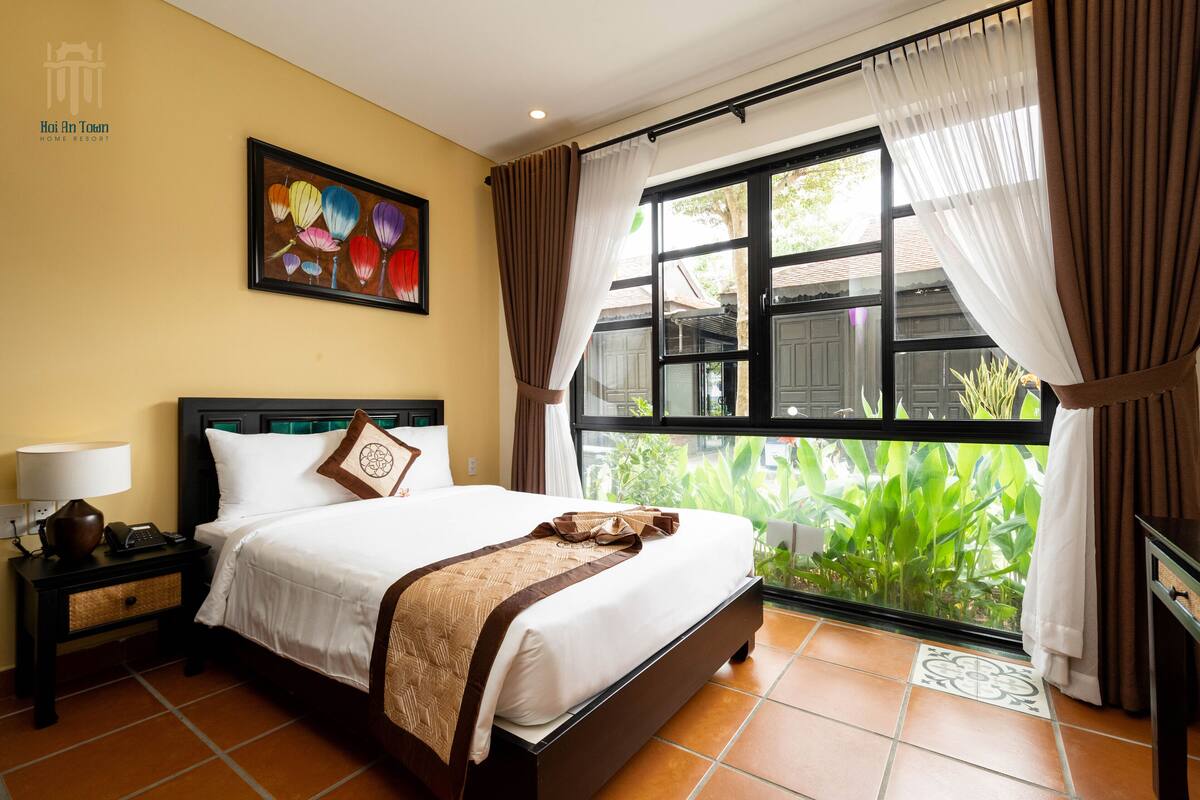 A hotel room with a bed, nightstand, lamp, and a window with curtains.