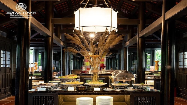 A buffet setup in a traditional-style room with a central chandelier, tall wooden pillars, and a tiled floor. - Hoi An Town Home Resort (Da Nang)