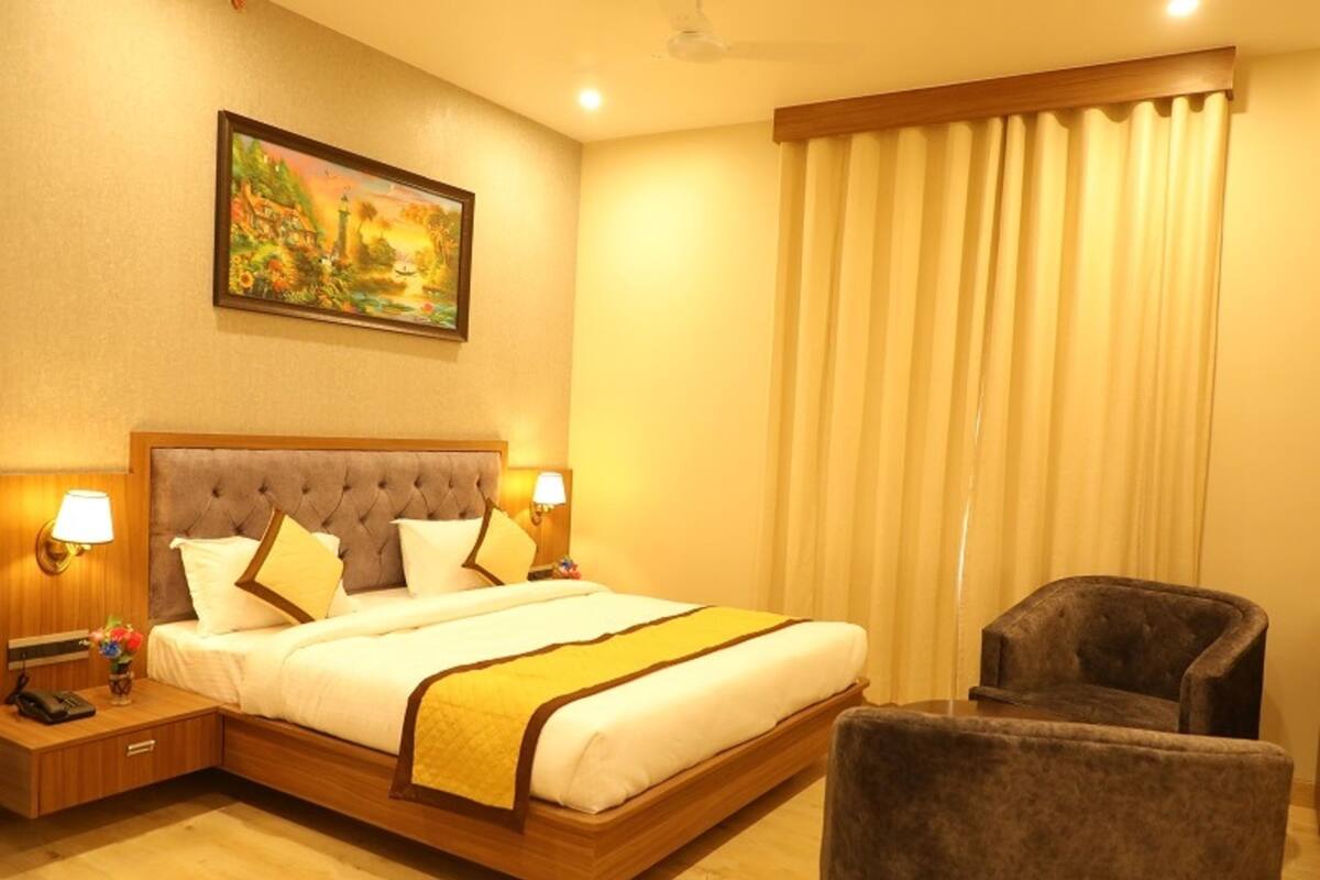 A hotel room with a large bed, two bedside lamps, a nightstand, a chair, and a painting on the wall.