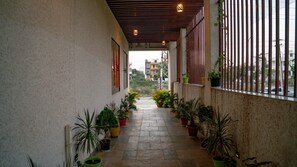A narrow corridor with potted plants on both sides, leading to a gate. - Pine Regency - Aravali's Peak view (Udaipur)