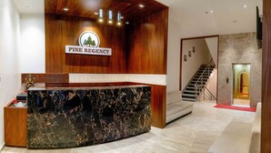A reception desk with a marble top, a wooden panel wall, and a staircase leading to an elevator. - Pine Regency - Aravali's Peak view (Udaipur)