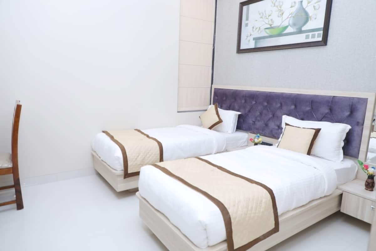 A hotel room with two beds, a chair, a nightstand with a vase of flowers, and a painting on the wall.