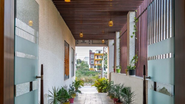 A corridor with potted plants, a tiled floor, and a view of buildings in the distance. - Pine Regency - Aravali's Peak view (Udaipur)