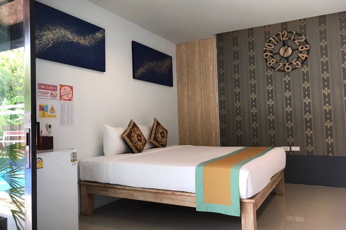 A bedroom with a wooden bed, two decorative pillows, a wall clock, and two framed artworks.