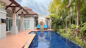 A swimming pool with two blue lounge chairs and a pergola structure.