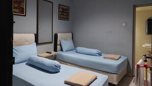 A room with two beds, each with a blue mattress and matching pillows, a wooden nightstand, and a wall-mounted air conditioner. - Pondok Seruni Kemanggisan Jakarta (Jakarta)