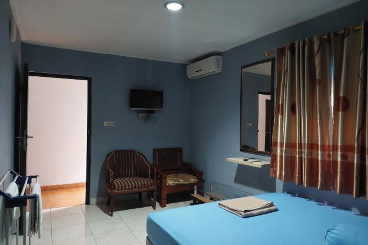 A bedroom with a bed, a chair, a television, an air conditioning unit, and a mirror.
