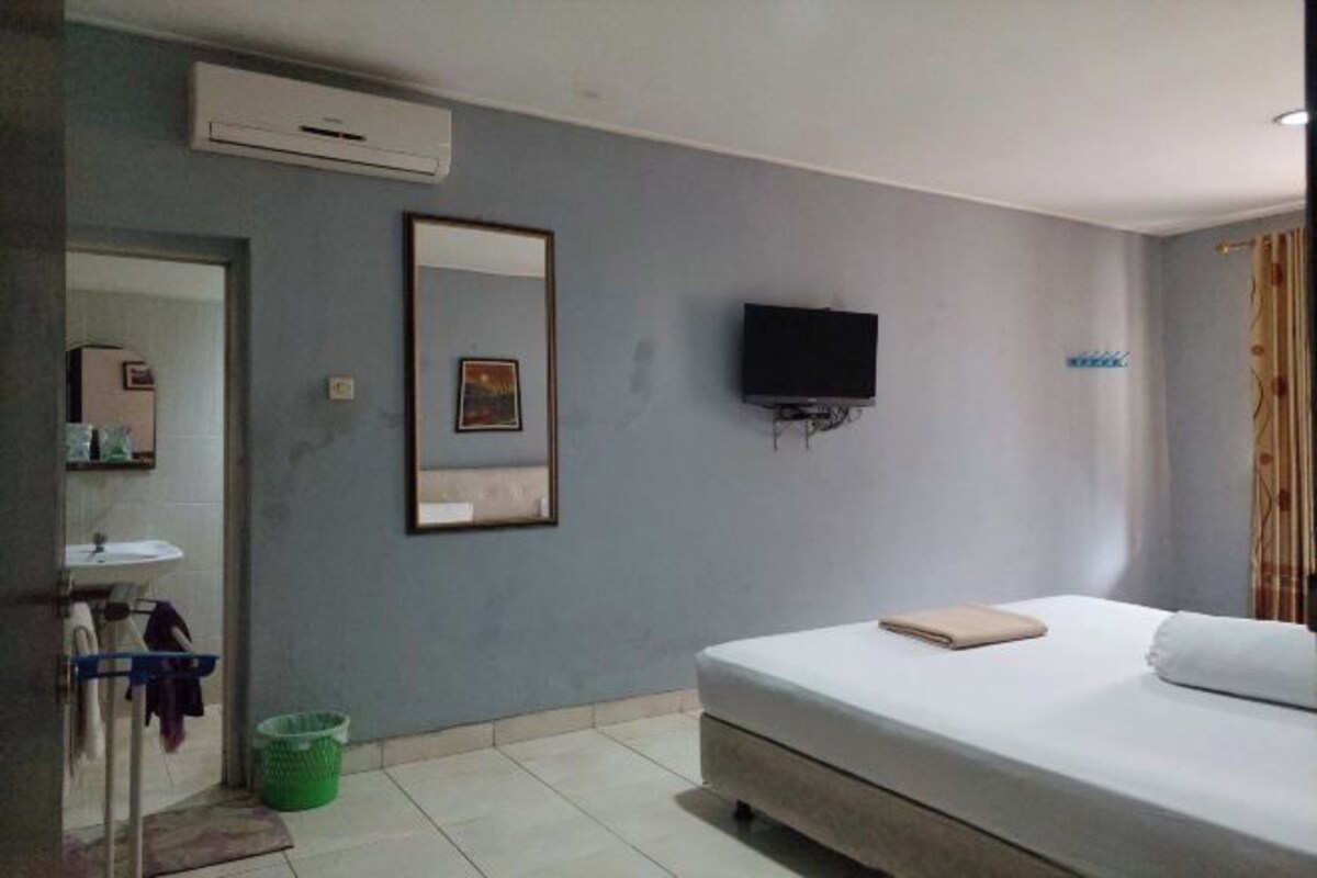 A bedroom with a bed, a television mounted on the wall, and a bathroom with a sink and mirror.