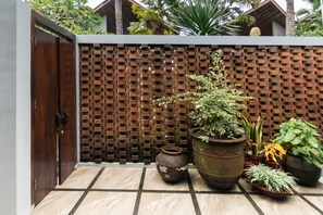 A tiled patio area with a wooden gate, a brick wall, and various potted plants. - Coco Ville Nusa Dua (Nusa Dua)