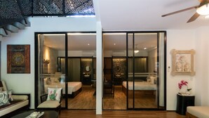 Una habitación de hotel moderna con suelo de madera, un sofá, una mesa de centro y una puerta corredera de vidrio que da al baño.