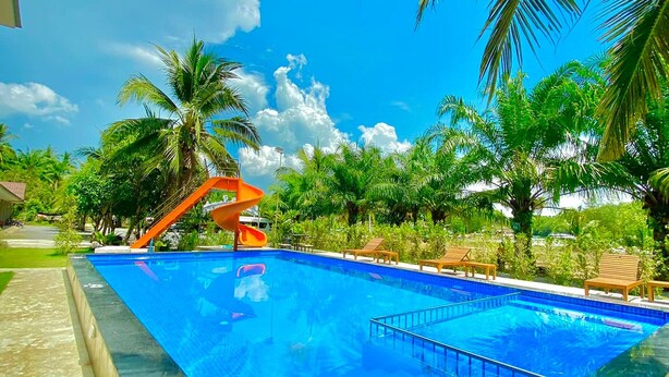 A swimming pool with a slide, surrounded by palm trees and lounge chairs. - Chanpailin Omarzaa (Krabi)