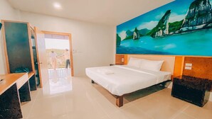 A hotel room with a bed, a desk, and a painting of a coastal landscape. - Chanpailin Omarzaa (Krabi)