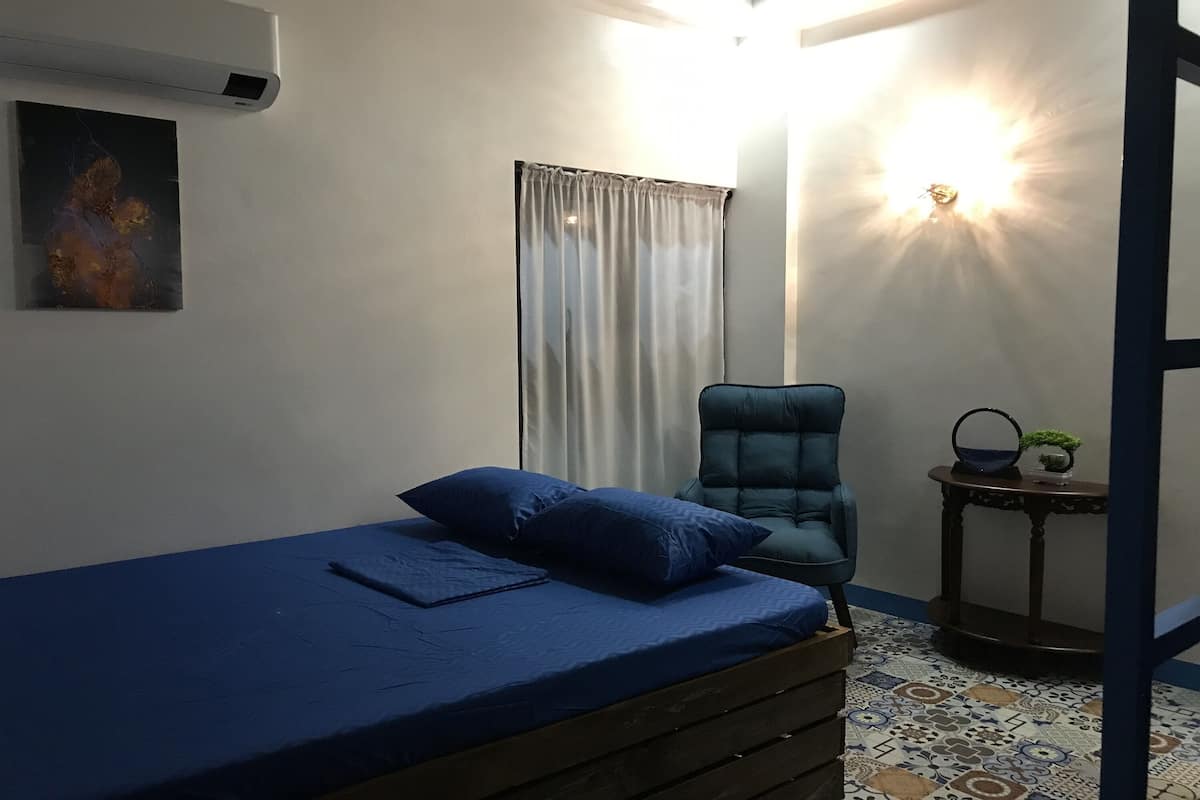 Une chambre à coucher comprenant un lit, une chaise, une petite table et un climatiseur fixé au mur.