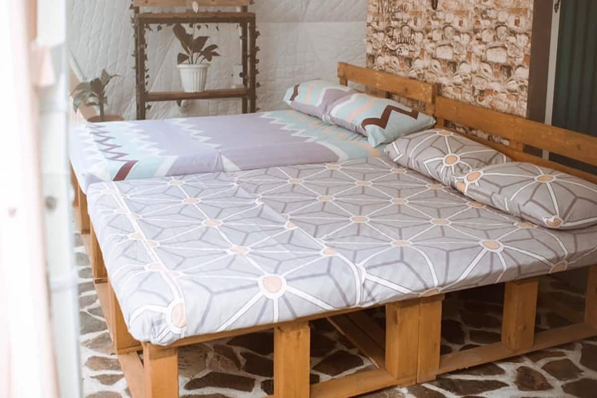Un lit avec une couvre-lit et des oreillers à motifs géométriques, une tête de lit en bois et un sol en pierre.