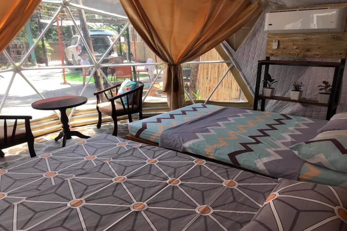 Une pièce confortable avec un lit, une petite table et des chaises. Il y a une fenêtre avec des rideaux et une étagère avec des plantes.