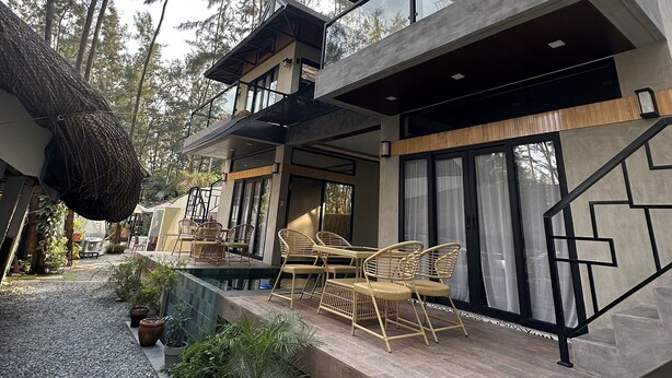 Una casa moderna de dos pisos con un patio, mobiliario exterior y vistas a altos árboles.