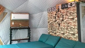 Una habitación acogedora con una cama, aire acondicionado de pared y una pared decorativa de ladrillo con un letrero de bienvenida.