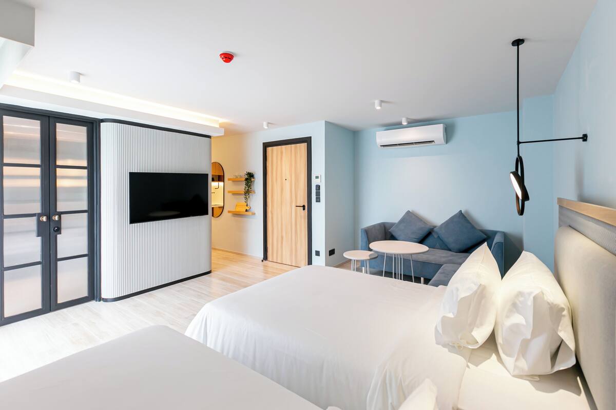 A modern hotel room with a large bed, a sofa, a TV, and a sliding door.
