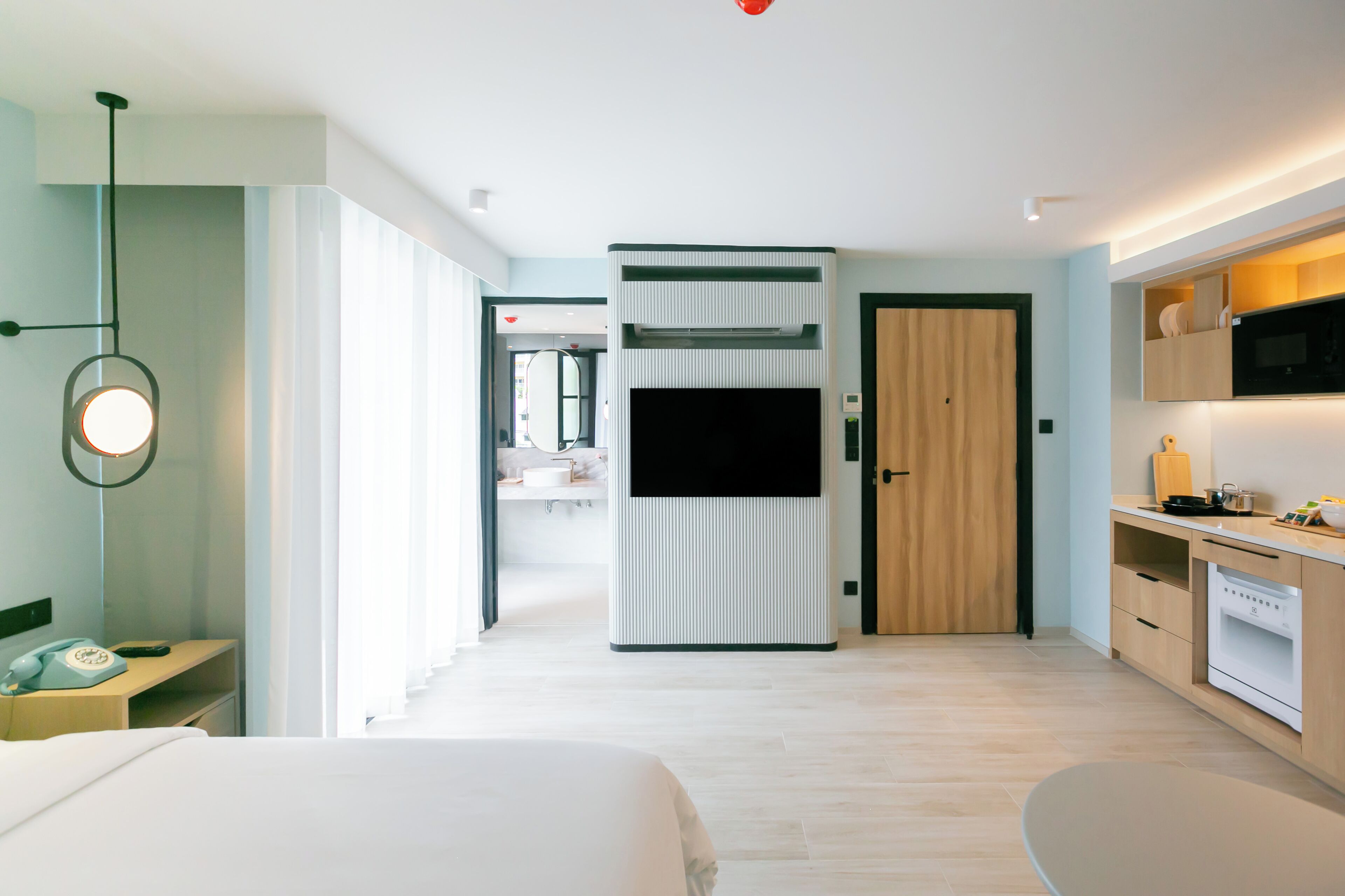A modern hotel room with a bed, bedside table, lamp, and a view of the hallway.