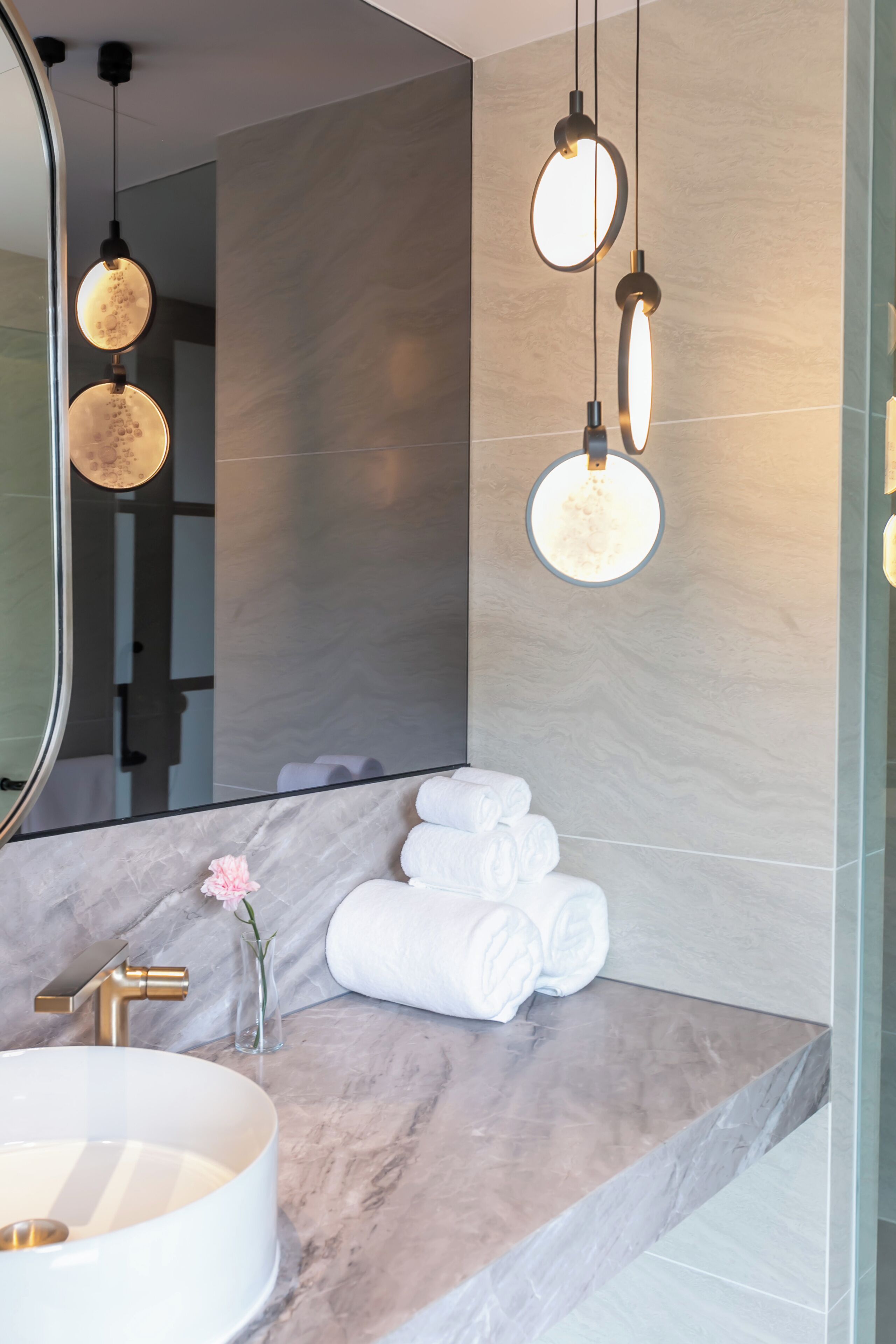 A modern bathroom with a marble countertop, a round sink, and a large mirror.