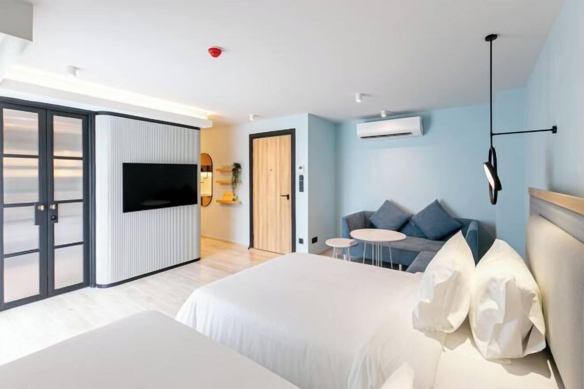 A modern hotel room with a large bed, a TV, a sofa, and a small table.
