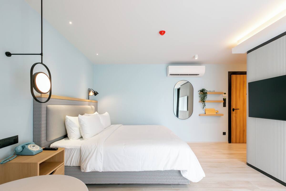 A modern hotel room with a bed, bedside table, lamp, mirror, and a TV.