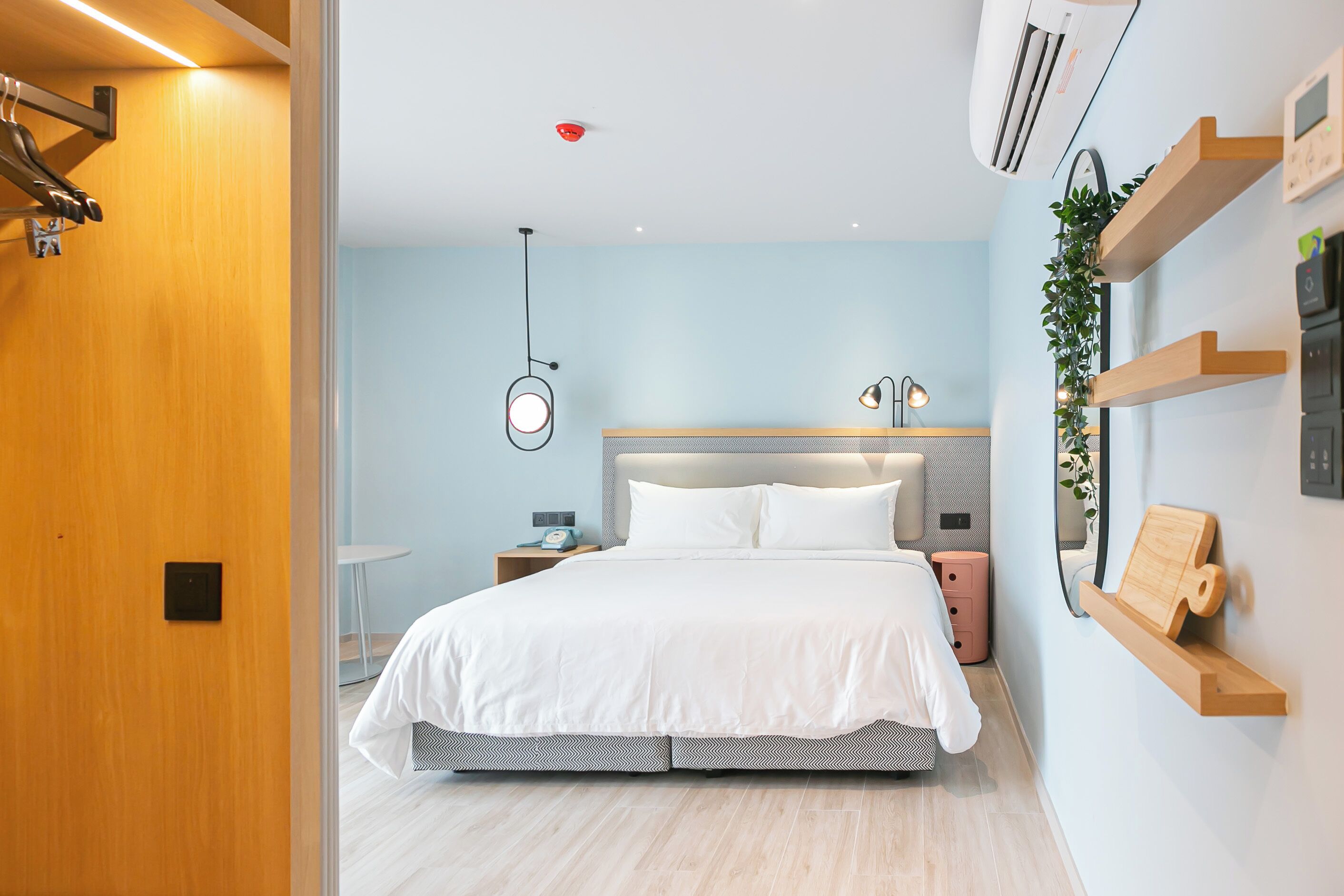 A modern bedroom with a bed, bedside tables, a wall-mounted shelf, and a ceiling-mounted air conditioner.