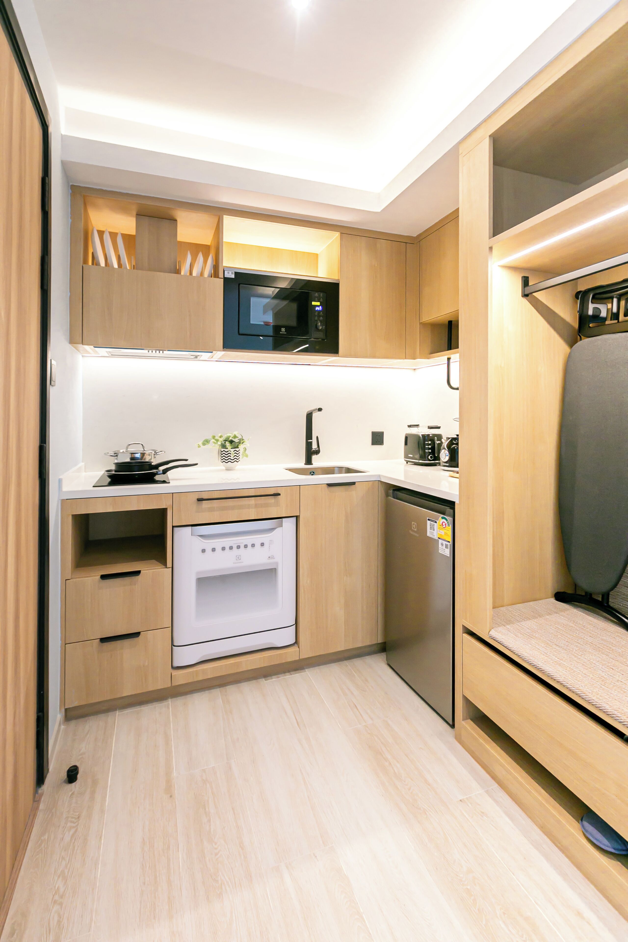 A compact kitchen with wooden cabinets, a microwave, a toaster, and a dishwasher.