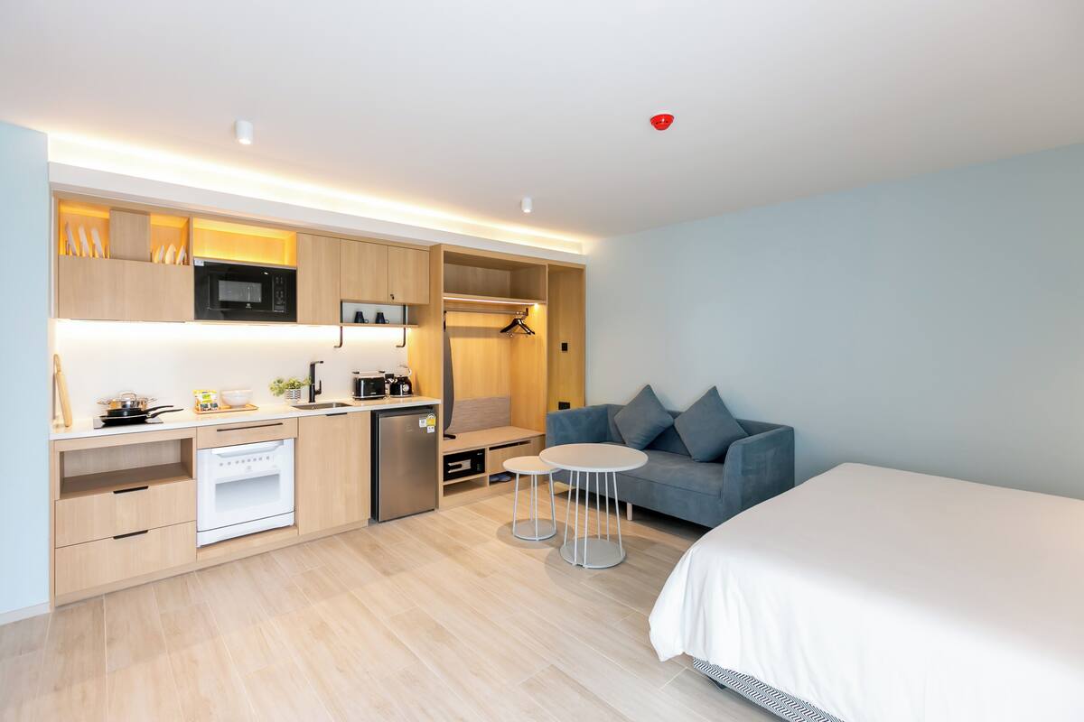 A modern hotel room with a kitchenette, a bed, a sofa, and a small table.