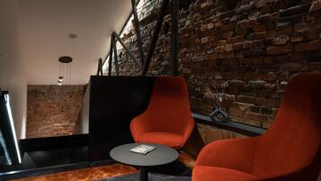 A modern interior with brick walls, a black partition, and two orange chairs around a small table.