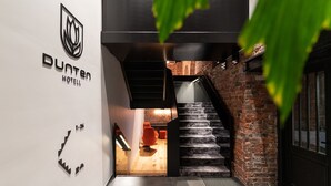 A modern hotel interior with a staircase leading to a wooden-floored area, a visible staircase, and a logo on the wall. - Dunten Hotel (Tallinn)