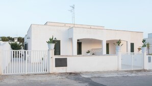 Un edificio moderno blanco con una entrada porticada, plantas en macetas y techo plano.
