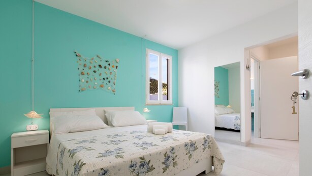 Un dormitorio con cama, mesitas de noche, una ventana y una puerta.