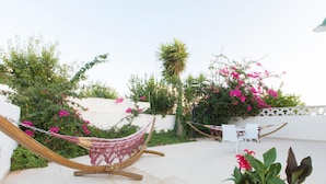 Una silla hamaca en un jardín con plantas en macetas y una pared blanca.