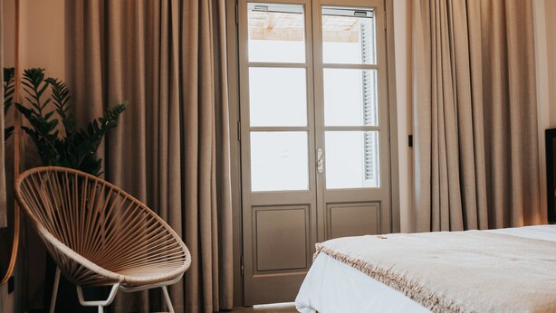 Un dormitorio con cama, una silla, cortinas y una puerta.