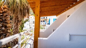 Un balcón de madera con un muro blanco y vistas a edificios al fondo.