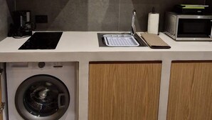 Una cocina compacta con armarios de madera, lavadora integrada, microondas y encimera con lavabo.