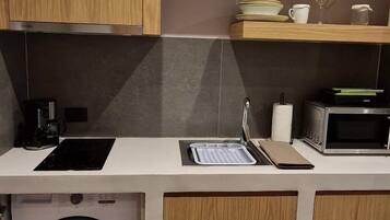 A compact kitchen with wooden cabinets, a built-in washing machine, a microwave, and a countertop with a sink.