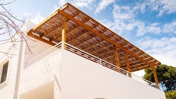 A building with a white exterior, a wooden pergola on the upper level, and a clear blue sky in the background.