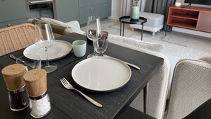 A dining table set with plates, glasses, and cutlery, a kitchen in the background, and a TV stand with a flat-screen TV. - New vacation cottage in the idyllic Ilz valley. 5 minutes to Passau (Salzweg)