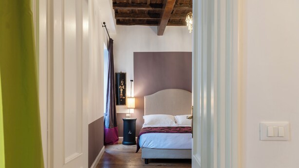 Ein schmaler Flur führt zu einem Schlafzimmer mit einem Bett, einem Nachttisch und einer Lampe.